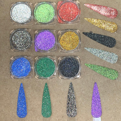 Nine containers from the Reflective Glitter Set by Dynamic Nail Supply, featuring silver, red, green, gold, black, blue, purple, and pink from the Super Sparkle - Disco Glitter collection, are arranged in three rows on a brown surface. Nearby are matching teardrop-shaped nail swatches that showcase the dazzling colors of these reflective glitters.