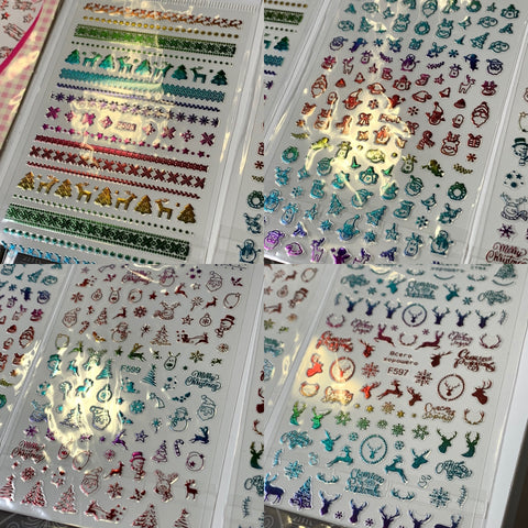 A Bundle of 20pcs Christmas Nail Stickers for $30 from Dynamic Nail Supply is elegantly presented, with each sheet featuring festive designs such as Christmas trees, snowflakes, snowmen, and reindeer. These shimmering metallic stickers come in red, green, blue, and purple shades and are organized neatly in rows and columns.