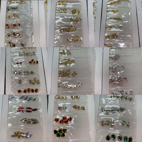 The display case is filled with rows of vibrant nail charms, similar to the assorted stud earrings it resembles. These Pre-made Nail Charms by Dynamic Nail Supply come in captivating designs such as butterflies, flowers, and abstract shapes. Adorned with colorful stones and crystals in shades of red, green, blue, and clear hues, each set is neatly arranged in clear transparent packaging.