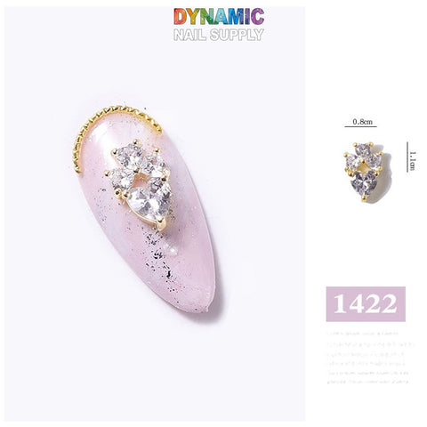 Close-up of a single artificial nail showcasing the Luxurious Jewelry for Nail Art design – part 4 from Dynamic Nail Supply. It features a pink base adorned with gold and silver embellishments and small clear gems arranged in an exquisite floral pattern. The luxurious, jewelry-inspired nail art measures 0.8 cm by 1.1 cm and includes product code 1422 at the top.