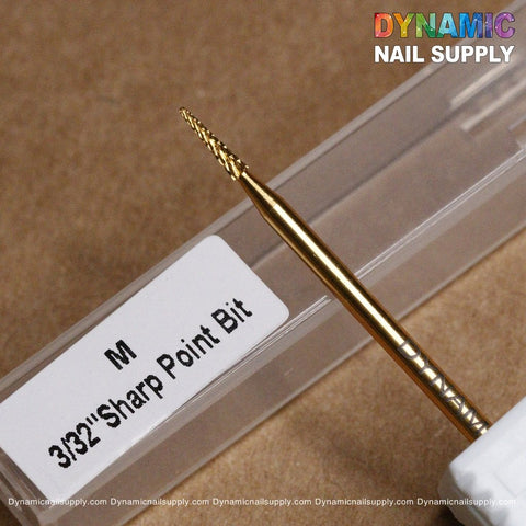 Close-up of a gold-colored Medium Sharp Point Bit - Dynamic Drill Bit, ideal for precise work around the cuticle area. It is positioned above its transparent plastic casing with the words Dynamic Nail Supply gleaming in rainbow colors at the top right corner, perfect for expert nail piercing tasks.