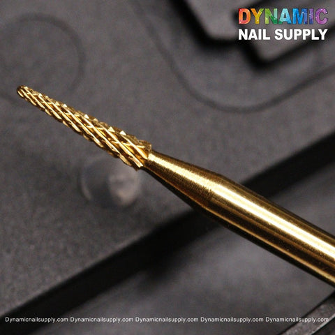 A close-up image showcases the "Medium Sharp Point Bit" from Dynamic Nail Supply, a gold-colored drill bit designed specifically for sealing the cuticle area. It features a textured spiral design set against a blurred black background. The brand name "Dynamic Nail Supply" appears in colorful letters at the top right corner, with their website listed below in small white text.