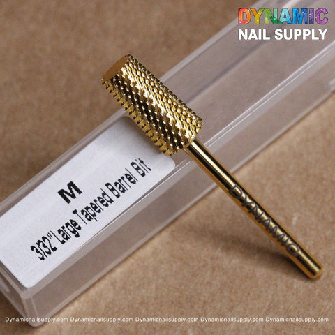 Close-up of the gold-colored M Tapered Barrel Bit - Dynamic Drill Bit, showcasing its large tapered barrel design, placed on a labeled plastic container. The label indicates it is a 3/32 large tapered barrel bit M. In the background, the Dynamic Nail Supply logo is displayed in colorful text.