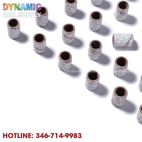 A set of light gray cylindrical sanding bands, essential for manicures, are displayed diagonally on a white background. The top left corner showcases the Dynamic Nail Supply logo, with their hotline number, 346-714-9983, prominently featured in bold red at the bottom.