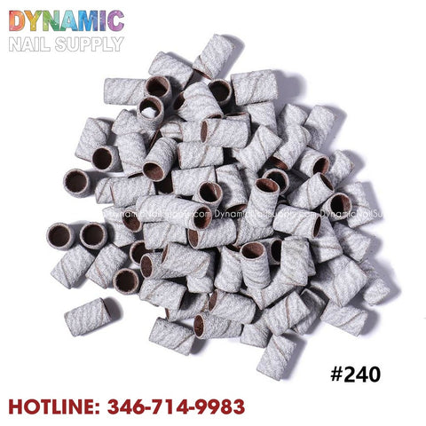 A collection of zebra-textured sanding bands, suitable for manicures, are arranged against a white backdrop. These cylindrical and hollow bands are labeled as Machine Nail Drill Bits Zebra Sanding Bands Foot Care Polishing Manicure Gel Polish Remover Replacement Tools Cutter. At the top, the brand name "Dynamic Nail Supply" is displayed in vibrant letters, accompanied by a hotline number and "#240" in red text beneath.