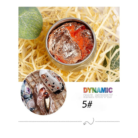 A compact tin containing crumpled silver and orange metallic foil resting on a bed of straw. Below, a round inset image highlights beautifully decorated nails featuring the foil. The bottom text reads "Dynamic Nail Supply" in colorful letters, perfect for enthusiasts of Big Size 14cm Nail Foil paper for Nail Art Design.