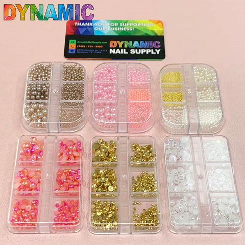 A set of six clear containers beautifully displays the Iridescent Pearl & Metallic Ball Bead for Nails Design, featuring captivating nail art decorations with pearls, beads, and rhinestones in pink, gold, and white hues. A business card from Dynamic Nail Supply is elegantly positioned on a pink textured surface, offering ideal inspiration for any nail designer.