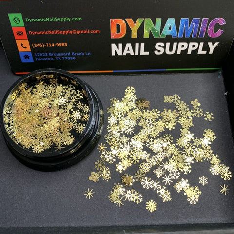 A small black container opens to reveal a collection of gold metallic snowflake and star-shaped embellishments, ideal for creating stunning Christmas nail art designs. In the background, you can see the Dynamic Nail Supply logo along with their contact details, including a Houston, TX address and phone number.