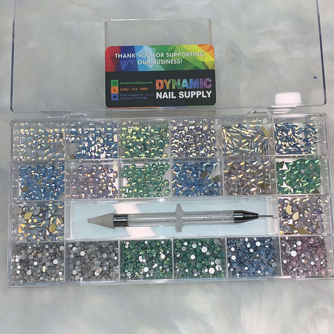 A set of [OPAL IRIDESCENT MULTI COLOR] rhinestones, housed in a clear plastic box with compartments, features a vibrant selection including shades of blue, green, pink, and silver. The set includes 14 big shapes and 6 round shapes. Inside the box rests a rhinestone picker tool. The lid is adorned with a Dynamic Nail Supply business card expressing gratitude for supporting their nail supply venture.