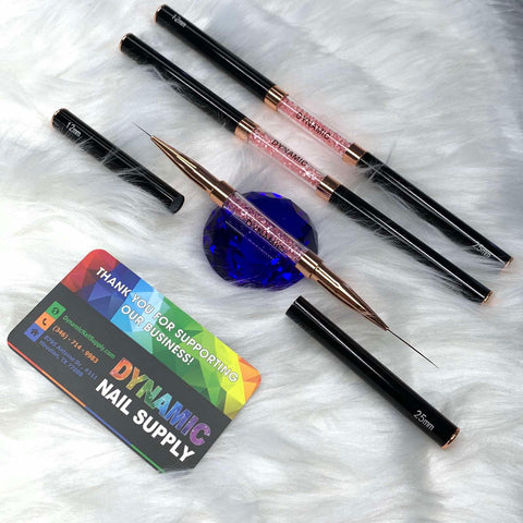 A set of Dynamic® Professional Dual-head Liner Brushes for fine lines is showcased on a fluffy white surface, featuring sizes 15mm, 20mm, and 25mm. Nearby rests an alluring blue glass gem and a business card from Dynamic Nail Supply, complete with contact details and a heartfelt thank you message.