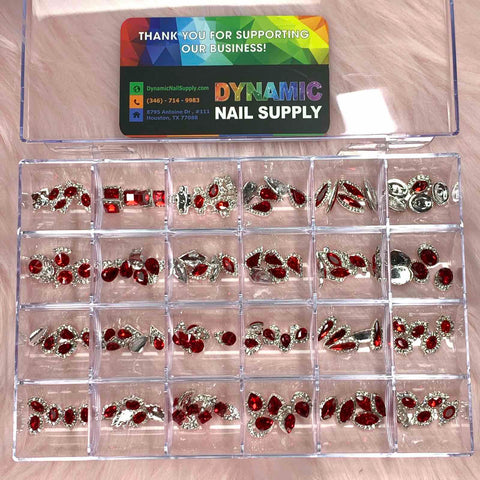 The 120 pcs Red Nail Charms set from Dynamic Nail Supply offers a plastic storage box that holds decorative nail gems, featuring vibrant red charms. Each compartment includes shiny silver and red rhinestone embellishments in various shapes and designs for creative nail art. Inside the lid, a business card for Dynamic Nail Supply is attached, showcasing contact information against a colorful background.