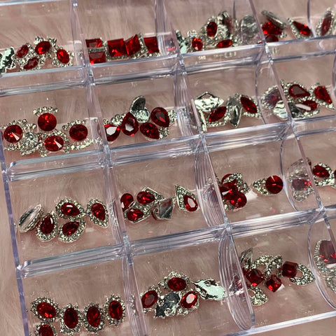 Close-up of the Dynamic Nail Supply's 120 pcs Red Nail Charms set, a transparent organizer box designed for nail art design. It features various compartments filled with red and silver gems in oval, round, and teardrop shapes. Each piece is beautifully set in sparkling silver settings, perfectly arranged for easy access.
