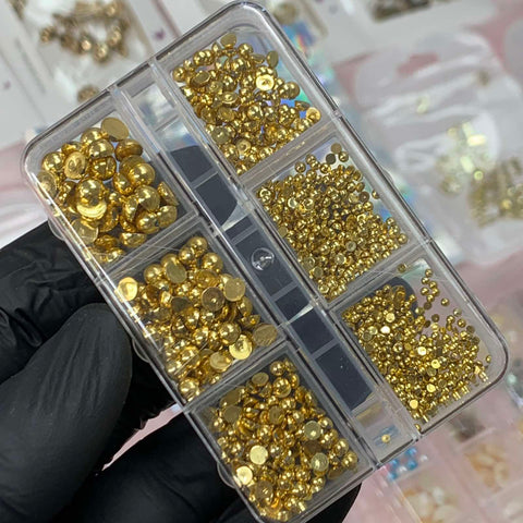 A hand wearing a black glove holds a transparent organizer filled with compartments of shimmering Iridescent Pearl & Metallic Ball Beads, ideal for any creative nails designer. In the background, slightly blurred, are various similar containers from Dynamic Nail Supply.