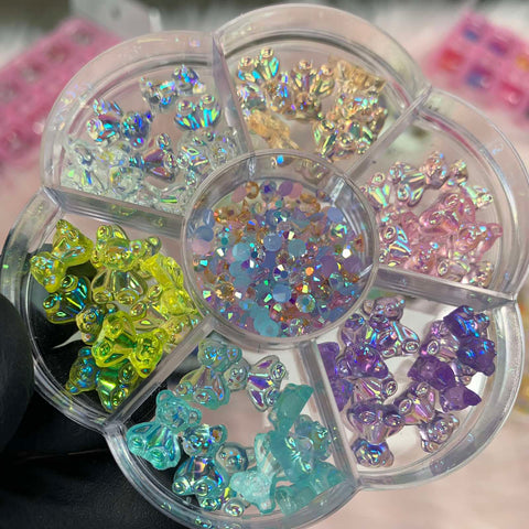 The Dynamic Nail Supply floral-shaped container is filled with 60 trendy 3D resin bear-shaped charms, ideal for any nail art designer. Each petal holds a charming bear in shades of yellow, light blue, pink, lavender, turquoise, and clear. The center compartment sparkles with small iridescent pastel rhinestones.