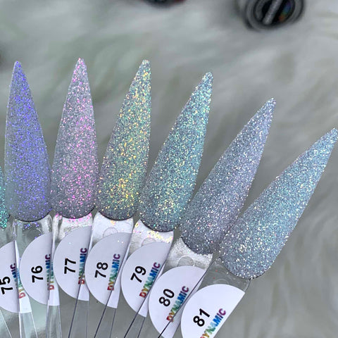 A close-up showcases six samples of Dynamic Nail Supply's Iridescent Loose Glitter (Super-Fine Size) for Sugar Nails Art Design, each uniquely labeled from 75 to 81. These sparkling, non-toxic nail polish shades exhibit a pointed shape and range in colors from pinkish to blueish tones, featuring a loose glitter finish. Set against a soft and fuzzy light gray background, they provide perfect inspiration for dazzling nail art creations.