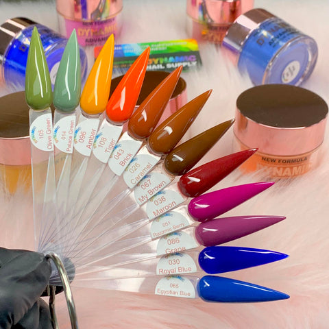 A vibrant fan-shaped display of 12 pointed nail polish swatches on transparent sticks showcases the "2024 Fall Acrylic Powder Collection (part 2) Newest" from Dynamic Nail Supply. The collection features a range of greens, oranges, browns, reds, purples, and blues. Each swatch is labeled and elegantly set against a soft pink background with accompanying jars of nail products for long-lasting wear.