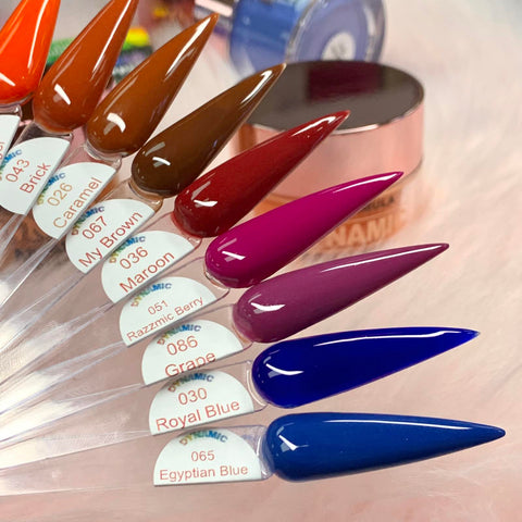 A close-up of six nail polish swatches displayed on elongated, pointed samples set against a soft pink backdrop. Featured in the 2024 Fall Acrylic Powder Collection (part 2) Newest by Dynamic Nail Supply, the colors are labeled as Caramel, My Brown, Maroon, Razzmic Berry, Grape, and Egyptian Blue. Each shade offers a glossy finish and ensures long-lasting wear.