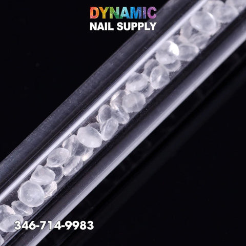A close-up of a clear tube filled with small, irregularly shaped rhinestones is shown diagonally against a glossy black background. The text "Dynamic Nail Supply" appears at the top in colorful letters, and the number "346-714-9983" is displayed at the bottom in white. This scene captures the essence of Dynamic Nail Supply's Dual-ended Nail Art Wax Dotting Pen Picking Up Rhinestone, perfect for nail art enthusiasts.