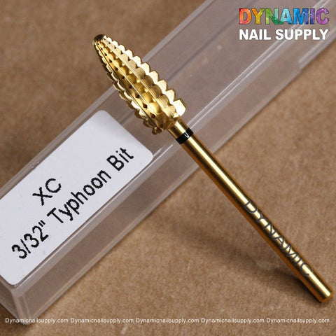 Close-up of a gold-colored XC Typhoon Bit - Dynamic Drill Bit labeled 3/32”, resting on a clear plastic case. The brand Dynamic Nail Supply is visible on the bit, and their colorful logo adorns the top-right corner of the image.